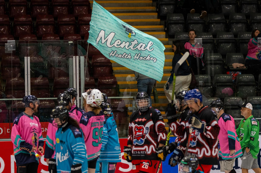 Hockey players holding a 'Mental Health Hockey' flag on an ice rink.