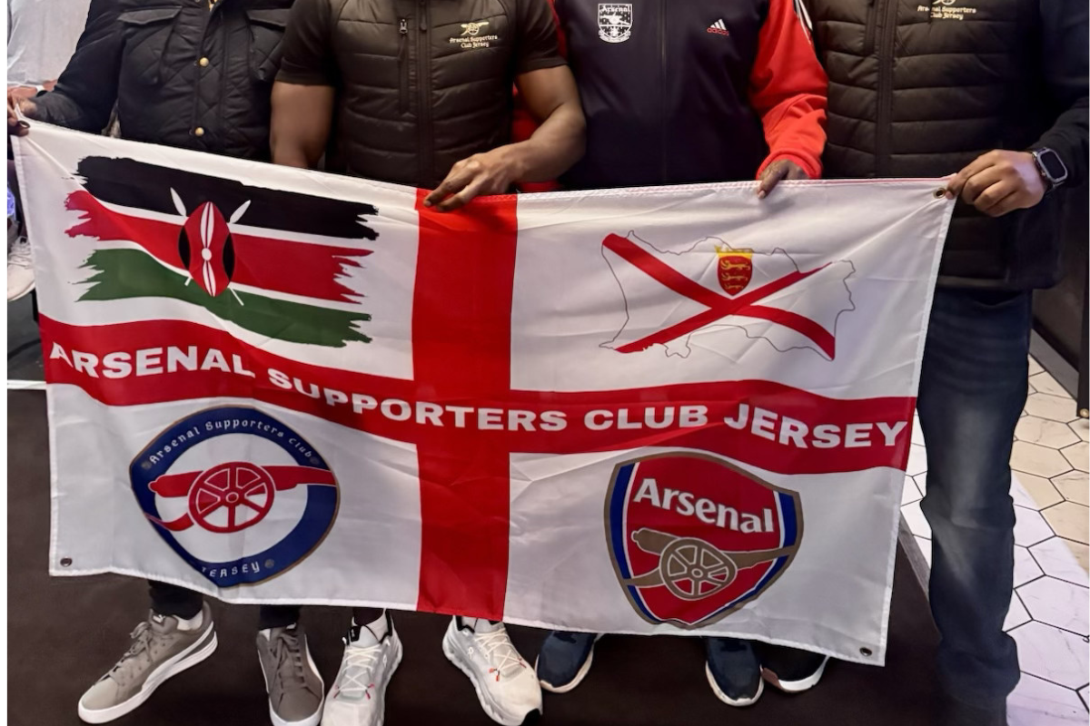 People holding an Arsenal supporters club jersey flag with team logos.